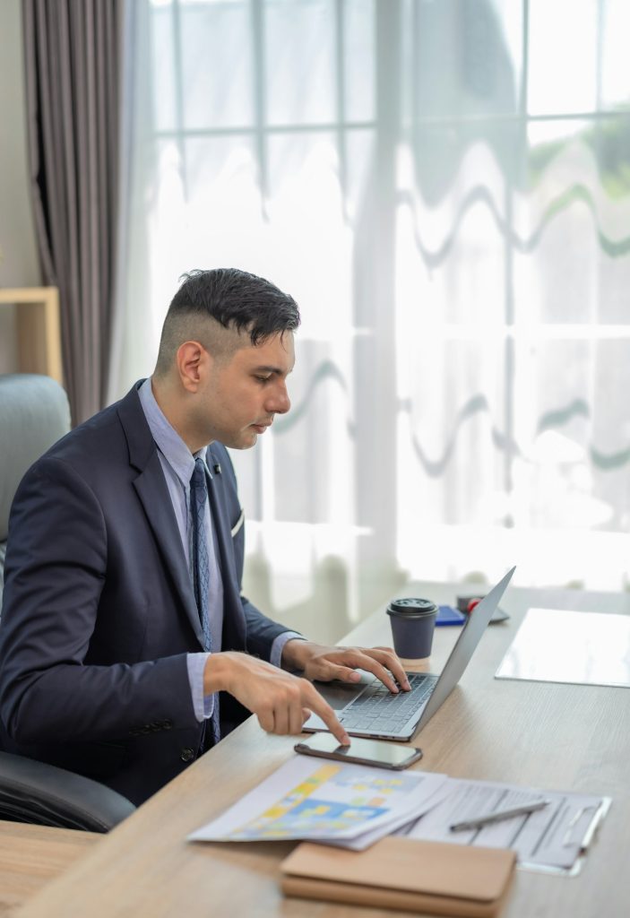 Male manager in suit multitask on laptop, tablet in modern office, talk to clients, analyze project